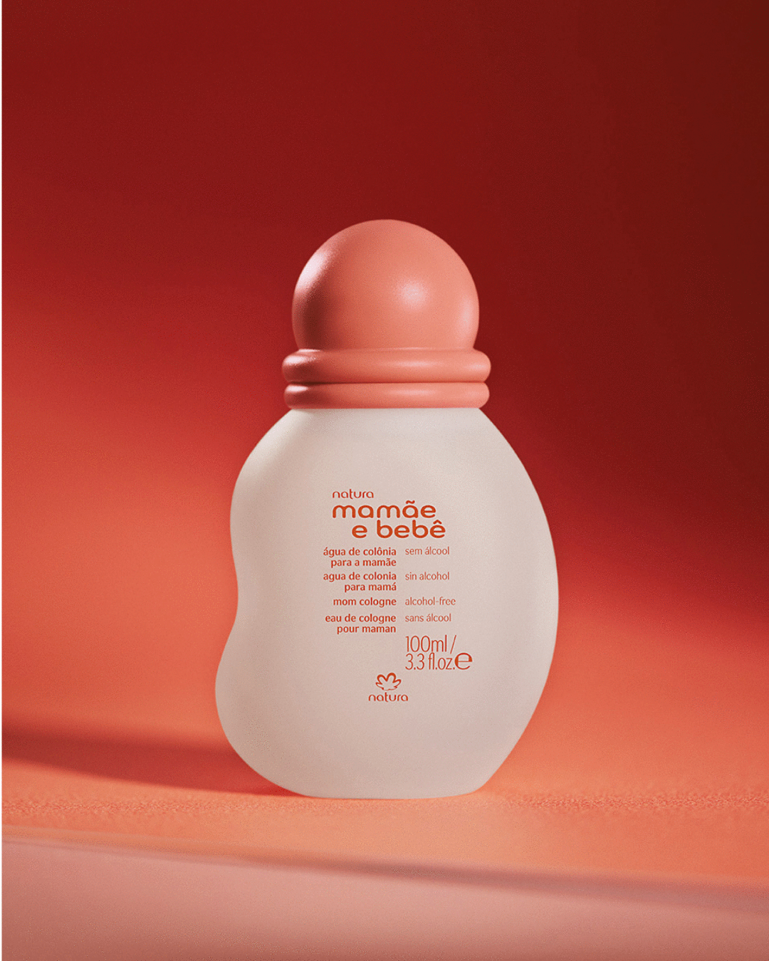Imagem de um frasco de colônia de cor leitosa,com a logomarca Mamãe e Bebê,a tampa e o fundo da imagem na cor coral 